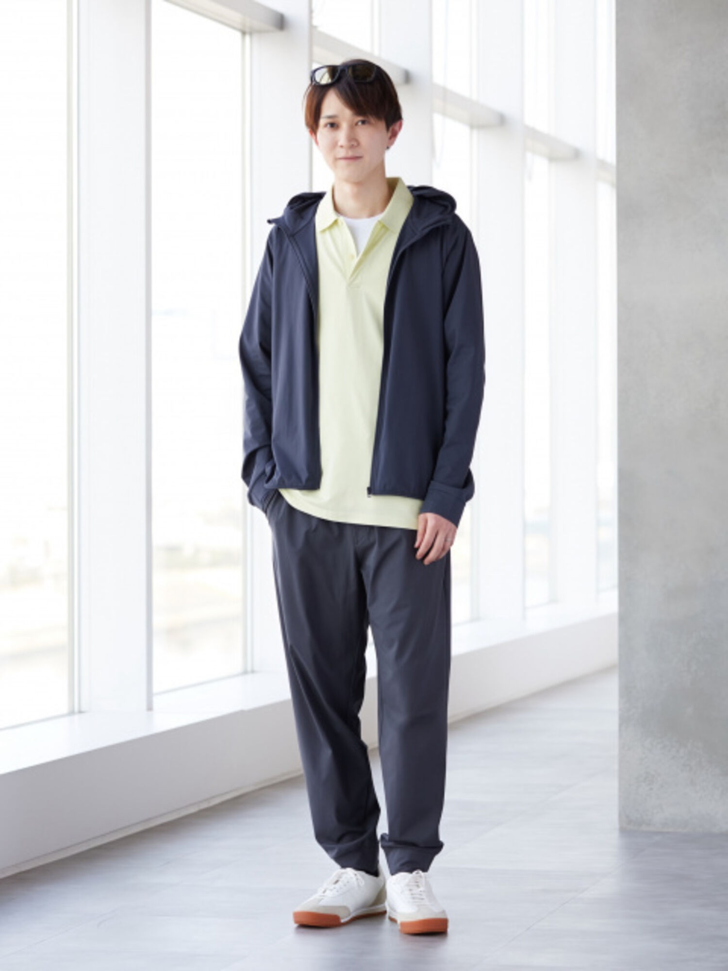 サングラスを頭に乗せ、淡いイエローのポロシャツにネイビーのパーカーとジョガーパンツを合わせた、爽やかな男性の全身コーディネート画像。