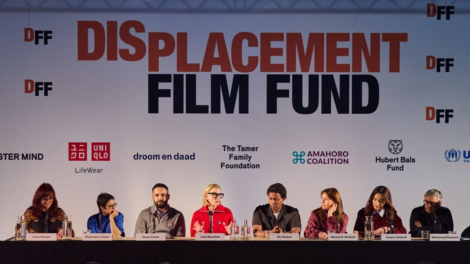 「DISPLACEMENT FILM FUND」の大きな文字と、ユニクロ等のロゴが並ぶ背景の前で行われた記者会見。