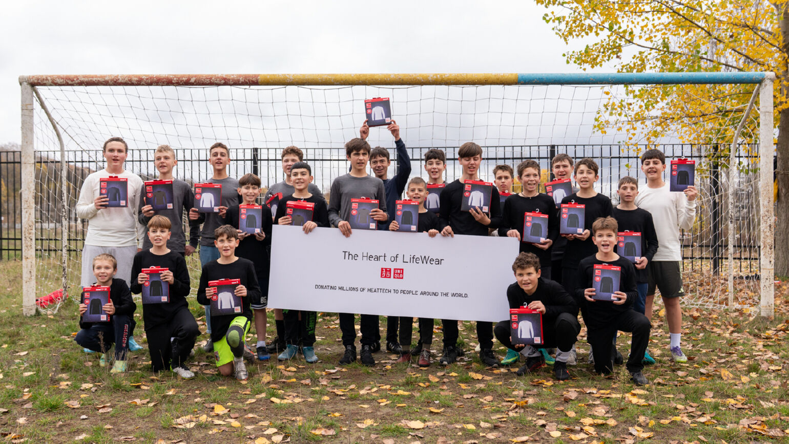 Group photo of a large number of children holding HEATTECH items in front of a football goal